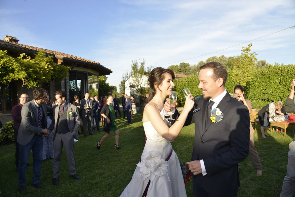 Gli sposi si guardano e brindano mentre gli invitati ballano in giardino